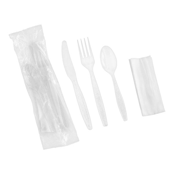A set of clear plastic cutlery including a knife, fork, spoon, a folded napkin, and a wrapped pack containing similar items, all arranged on a white background.
