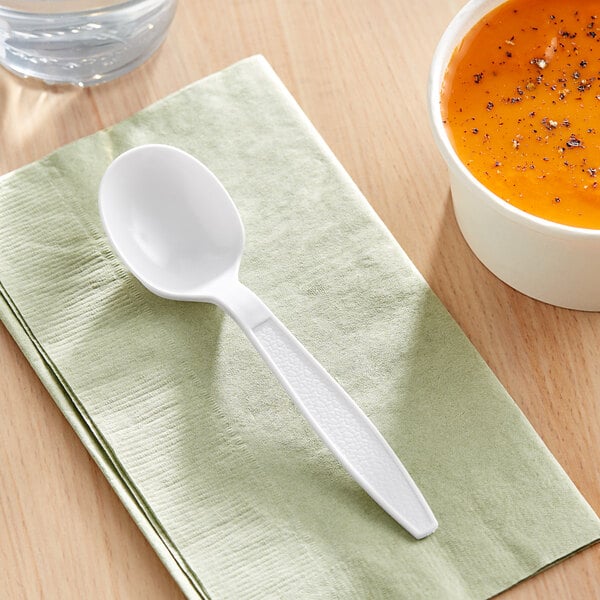 A white Choice plastic soup spoon on a napkin next to a bowl of soup.