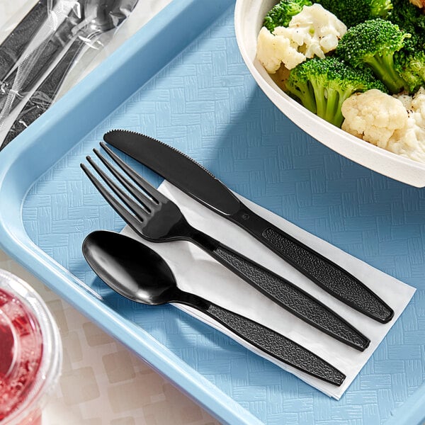 A tray with a bowl of broccoli and black utensils including a spoon and fork.