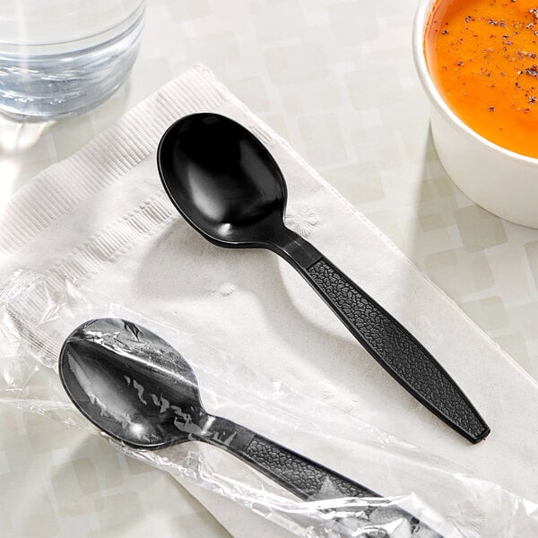 A black Choice heavy weight plastic soup spoon on a napkin.