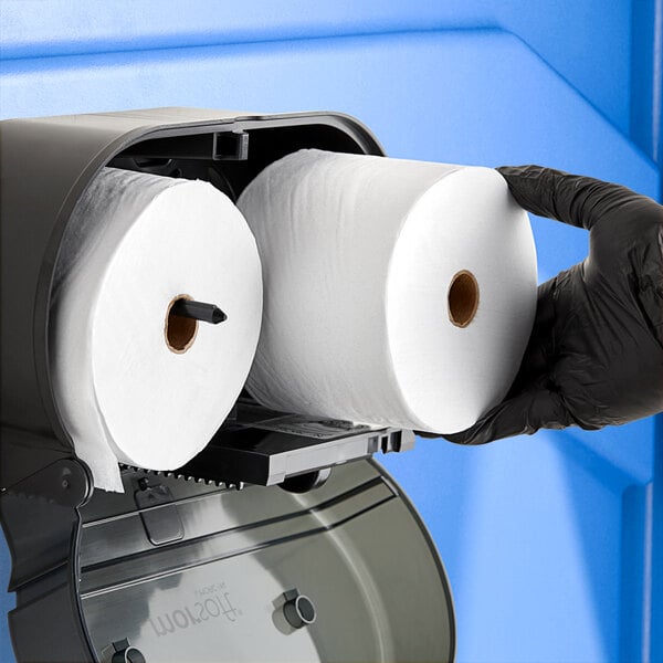 A person in black gloves holding a roll of Morcon standard high-capacity toilet paper.