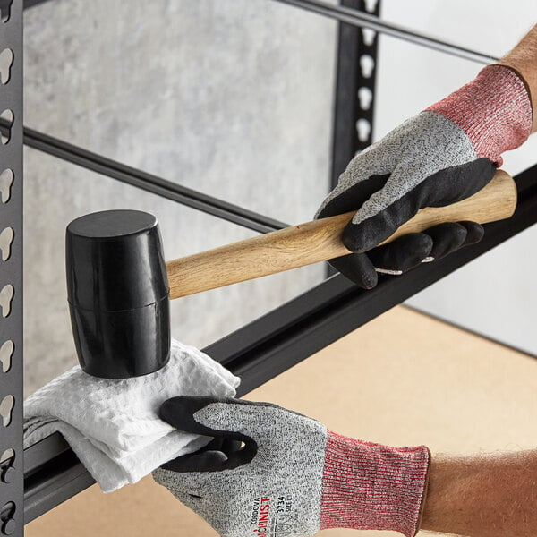 A person holding an Assure Parts rubber mallet over a metal bar.