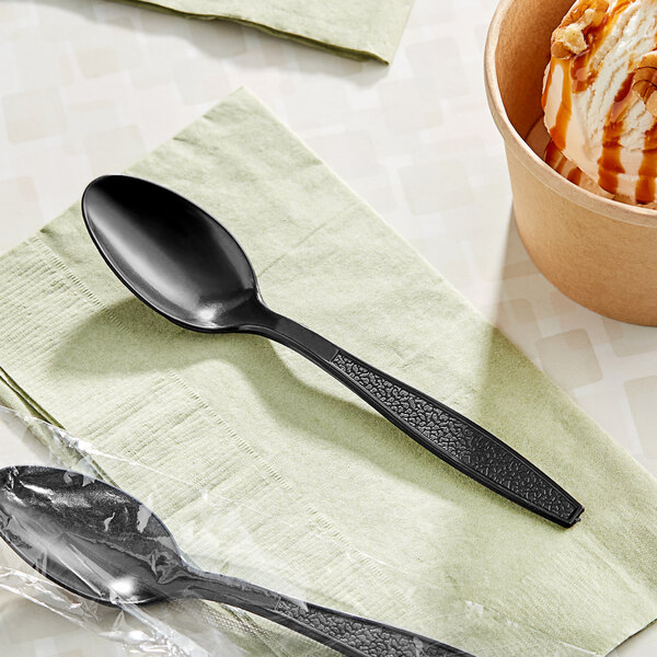 A black plastic wrapped Choice teaspoon with ice cream on a napkin.