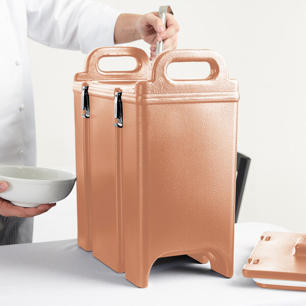 A person holding a bowl and a brown Cambro insulated soup container.