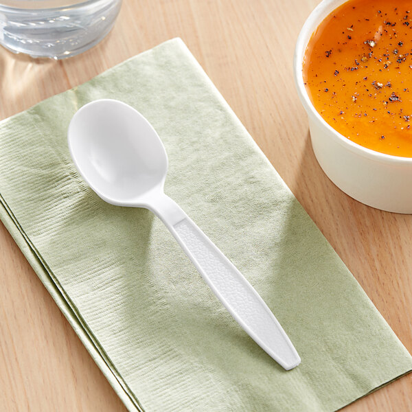 A white plastic soup spoon on a napkin next to a bowl of soup.