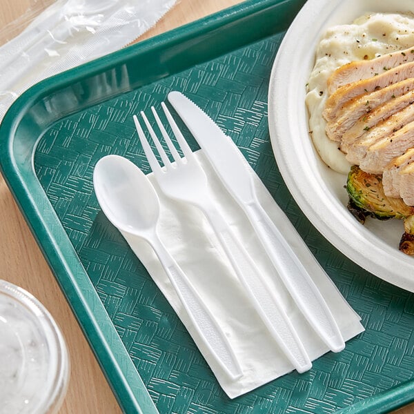 A tray with a plate of food and white plastic utensils including a spoon and napkin.