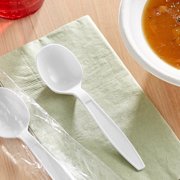 A white plastic soup spoon on a table with a bowl of soup.