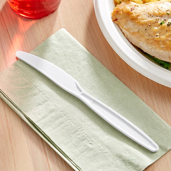 A white plastic Choice heavy weight knife on a green napkin next to a plate of chicken.