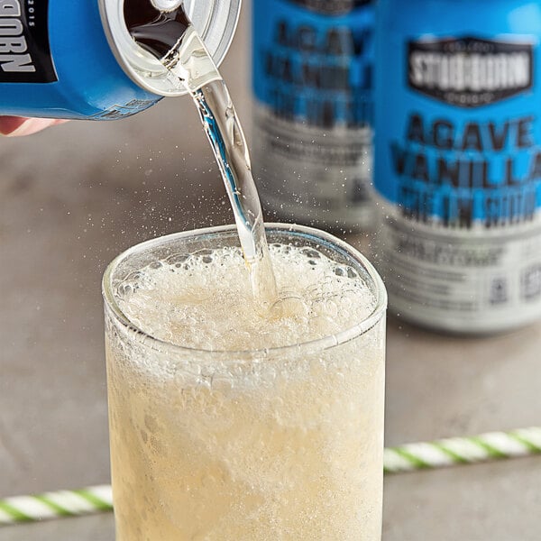 A person pouring Stubborn Agave Vanilla Cream Soda into a glass with a straw.
