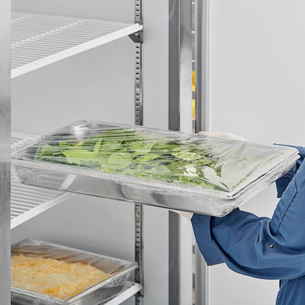 A person in a blue uniform holding a Vollrath stainless steel steam table pan full of food.