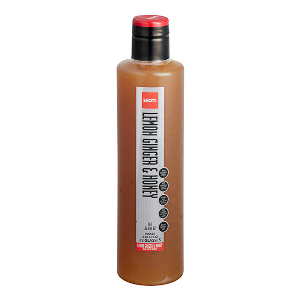 A close up of a SHOTT Lemon, Ginger, and Honey syrup bottle with a red cap.