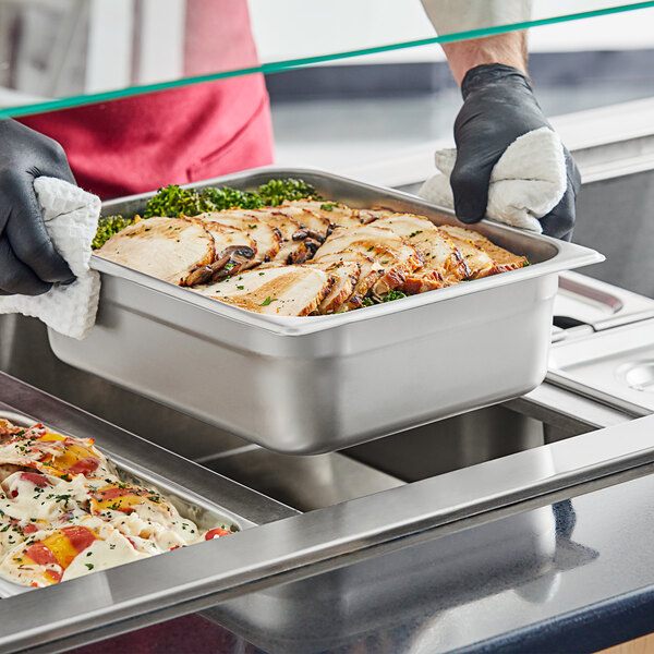 A person in gloves holding a stainless steel tray of food with meat and vegetables.