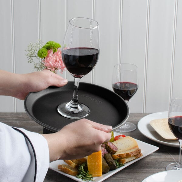 A person holding a Cambro non-skid serving tray with a glass of wine.