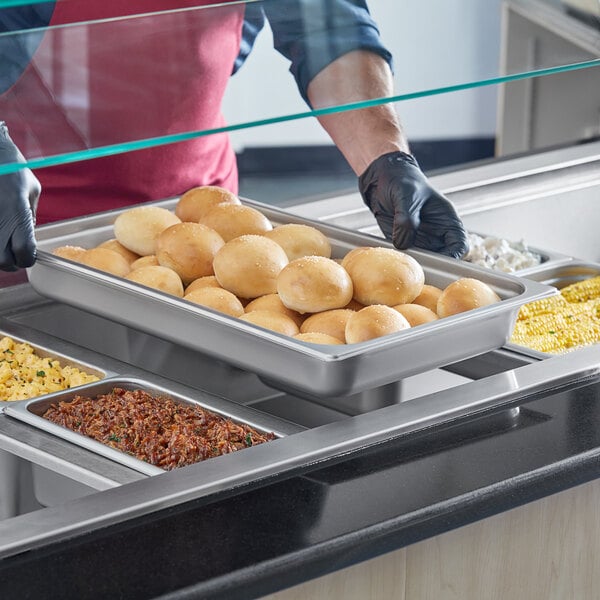 A man in a black apron using a Choice stainless steel steam table pan to prepare food on a counter.