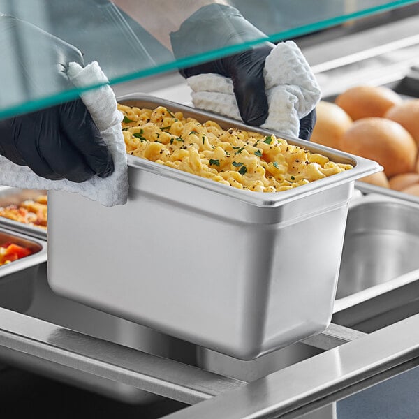 A person in black gloves holding a Choice stainless steel steam table pan with food in it.