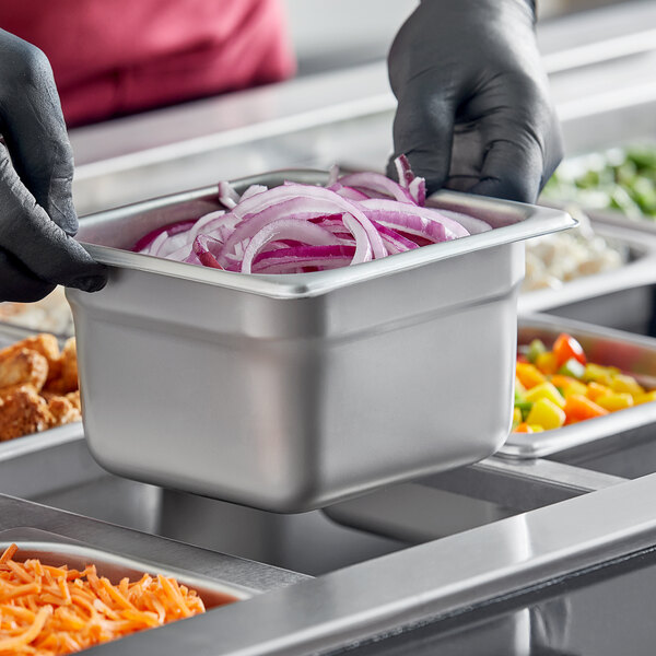 A person in gloves holding a Choice stainless steel steam table pan filled with food.