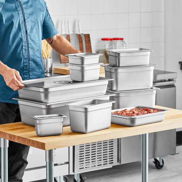 A man holding a stack of stainless steel Choice steam table pans.