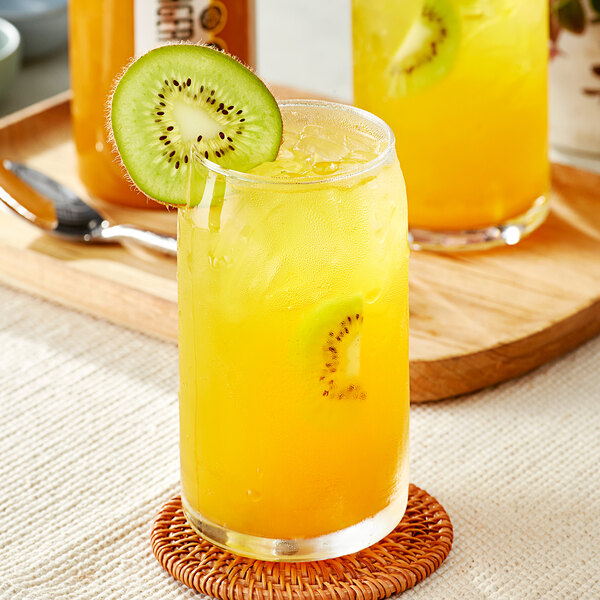 A glass of orange juice with SHOTT Gold Kiwi syrup and a kiwi slice on the rim.