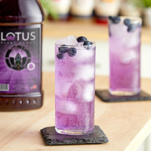 A glass of Lotus Plant Power Purple Lotus Concentrate with ice and blueberries.