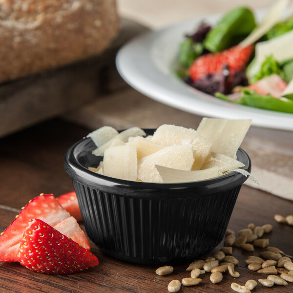 A black fluted Carlisle ramekin filled with cheese on a table with a salad.