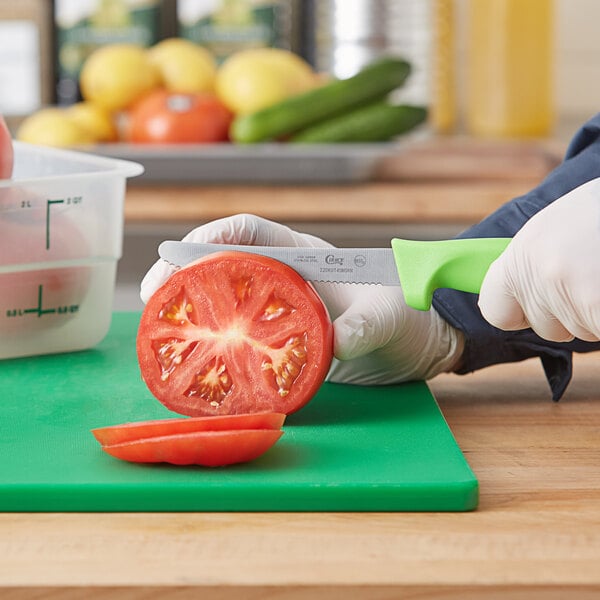 A person holding a Choice serrated utility knife and cutting a tomato.
