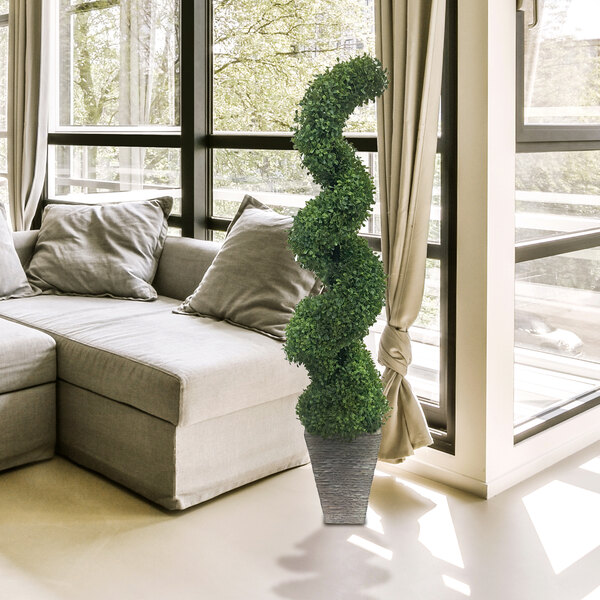 An LCG Sales artificial spiral topiary shrub in a faux stone pot in a room with a couch and pillows.