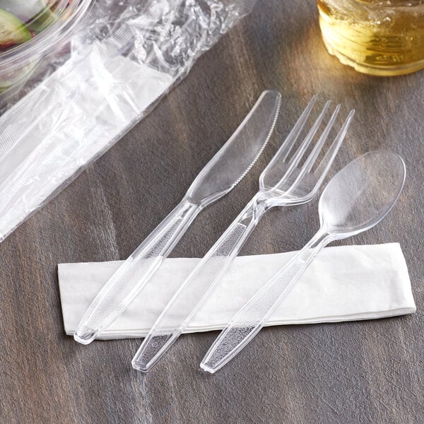 A Choice clear plastic fork, spoon, and knife wrapped in a napkin.