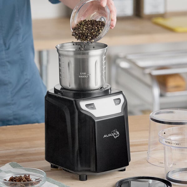 A black AvaMix commercial spice grinder with a stainless steel bowl being filled with whole spices.