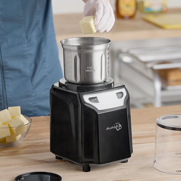 A black AvaMix commercial spice grinder with a stainless steel bowl being loaded with cubed ingredients.