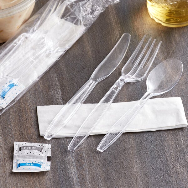 A clear plastic fork, knife, and spoon wrapped in a napkin with salt and pepper packets.