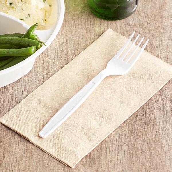 A white heavy weight plastic fork on a napkin next to a bowl of green beans.