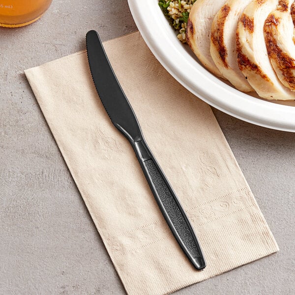 A Choice black plastic knife on a napkin next to a plate of food.