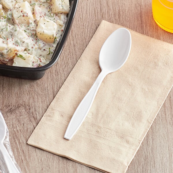 A white plastic spoon next to a bowl of potato salad.