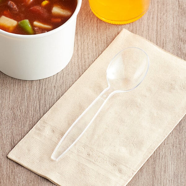 A clear heavy weight polystyrene plastic soup spoon placed on a beige napkin.