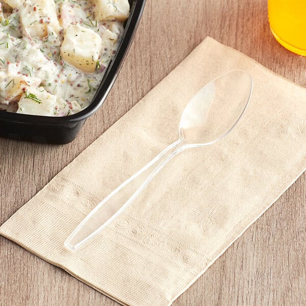 A clear heavy weight polystyrene plastic teaspoon placed on a beige napkin.