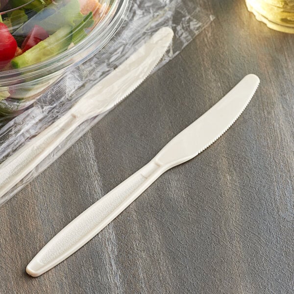 A wrapped beige plastic knife next to a bowl of salad.