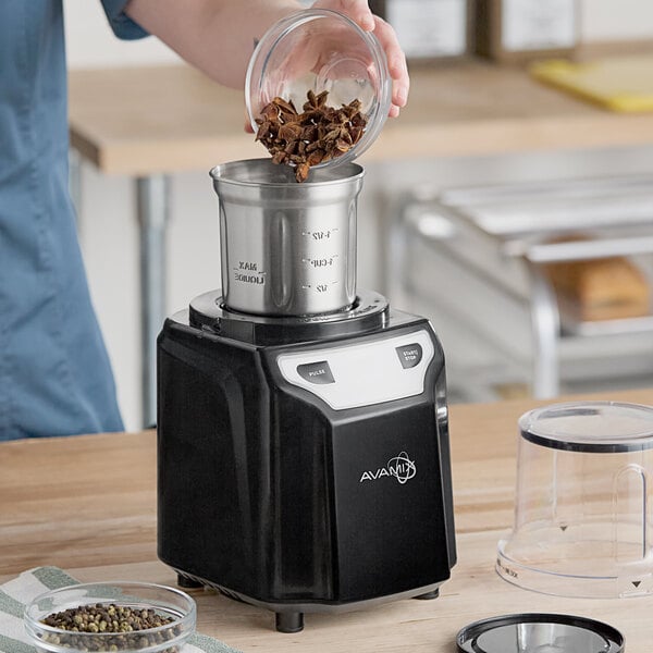A black AvaMix commercial spice grinder with a stainless steel bowl being filled with spices.