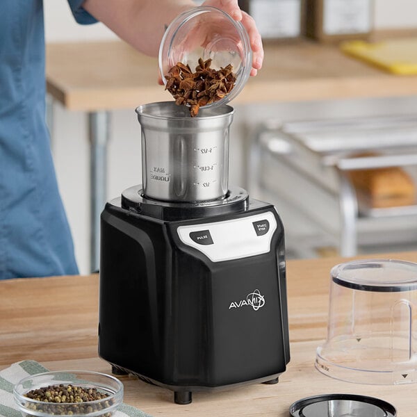 A black AvaMix commercial spice grinder with a stainless steel bowl being filled with spices.
