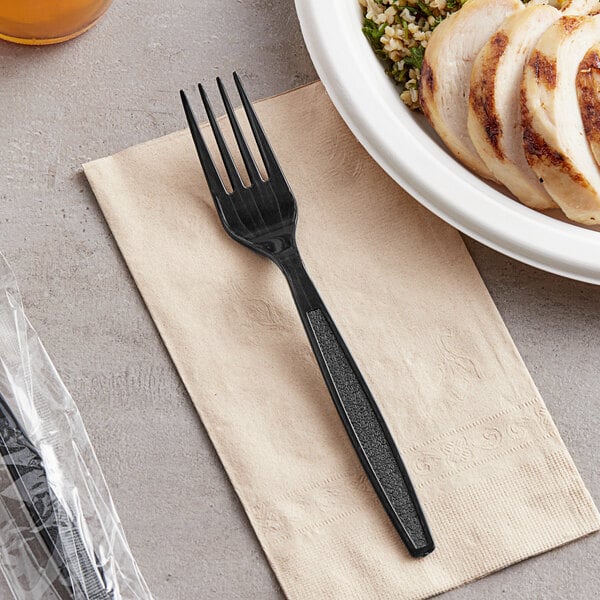 A black plastic wrapped fork on a table next to a plate of food.