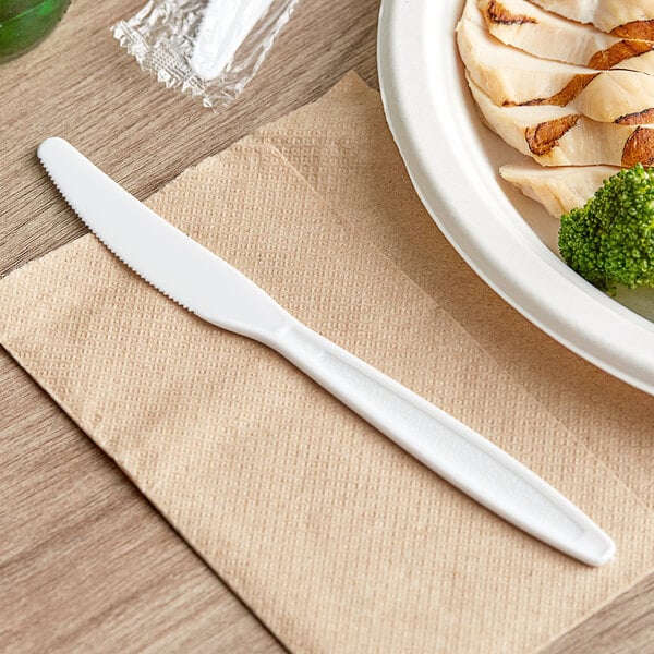 A white Choice heavy weight plastic knife on a napkin next to a plate of food.