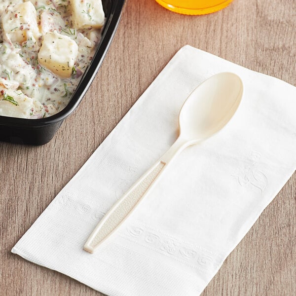 A beige plastic spoon next to a bowl of food.