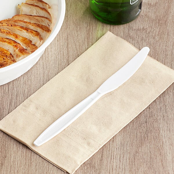 A white plastic Choice heavy weight knife on a napkin next to a bowl of meat.