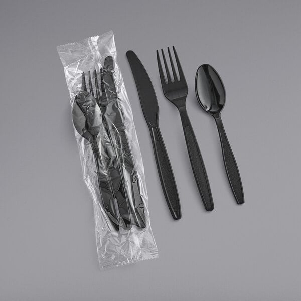 A plastic bag with black heavy weight plastic cutlery wrapped in black plastic.