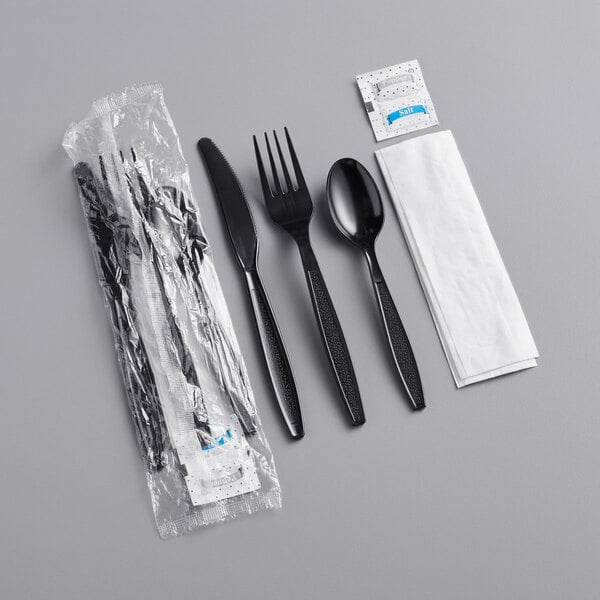 A black plastic wrapped cutlery set with napkin and salt and pepper packets.