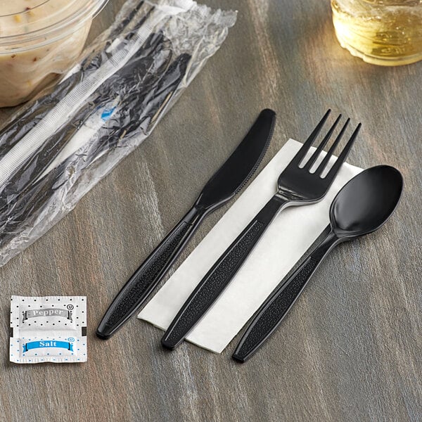 A black plastic fork and knife wrapped in a napkin on a table.