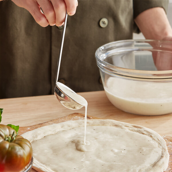 A person pouring Minor's vegan alfredo sauce onto a pizza dough.