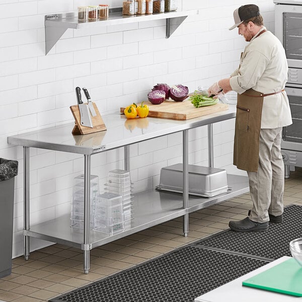 A man in a brown apron cutting vegetables on a Regency stainless steel work table.