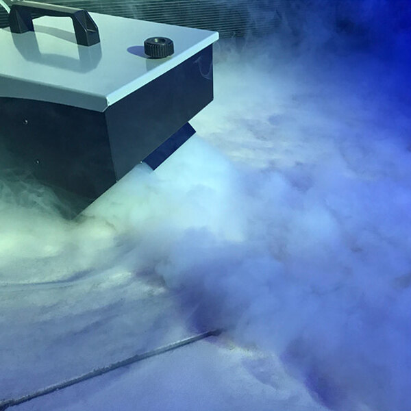 An American DJ Mister Kool II fog machine sitting on the floor with smoke coming out of it.