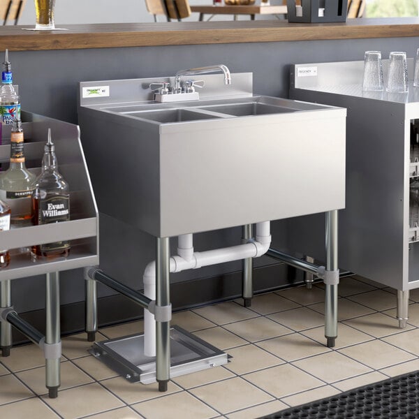 A Regency stainless steel underbar sink with two compartments on a counter in a cocktail bar.