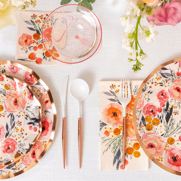 Sophistiplate Bella White / Blush plastic spoons, forks, and plates on a table with floral plates.